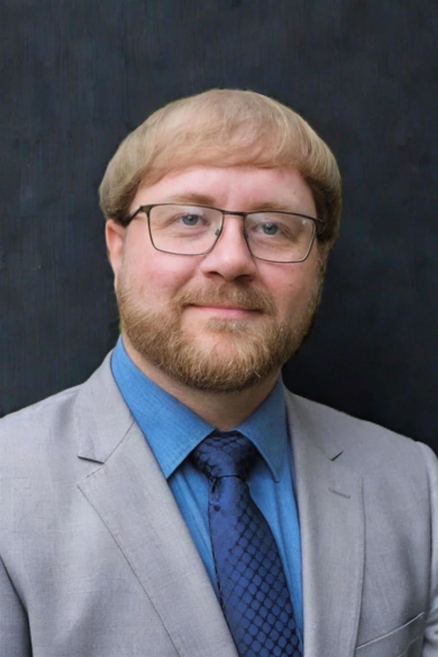  Patrick Smith is wearing glasses wearing a light gray suit and blue shirt.